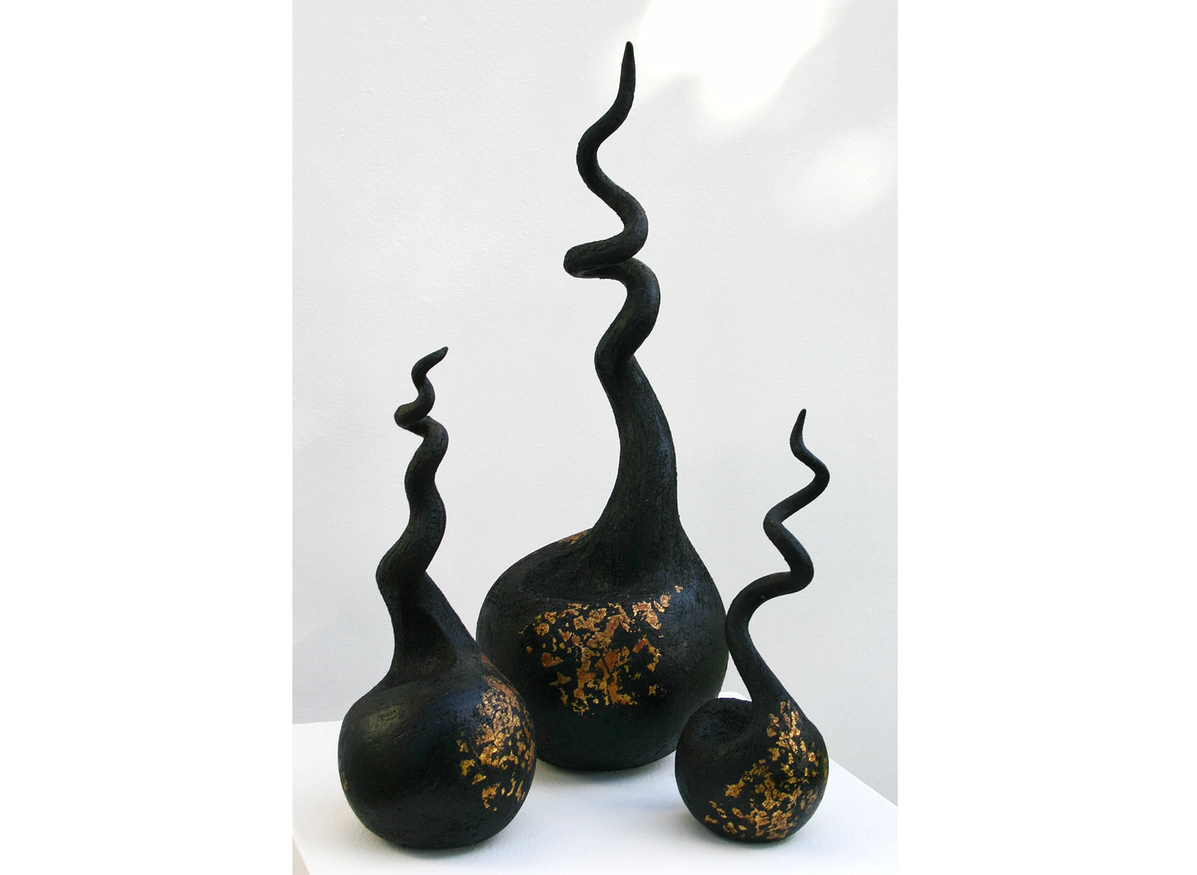 Three black curly sculptures of differing sizes decorated with gold leaf, called Black Triad